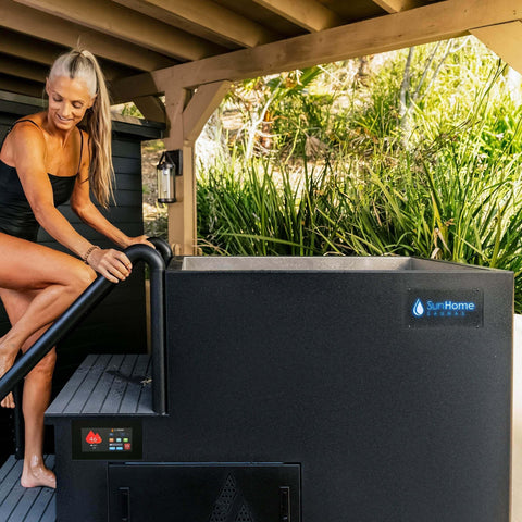 Woman steps onto the platform of the black Sun Home Cold Plunge Pro Apex tub, touch screen lit on front panel