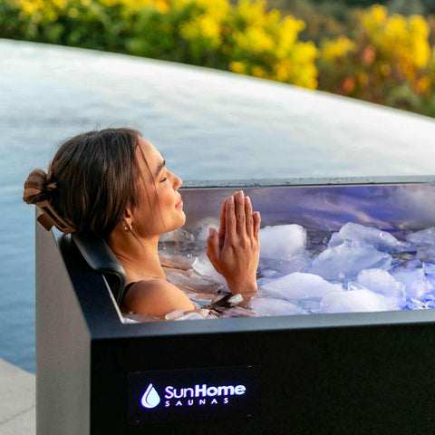 Woman resting in ice-filled Sun Home Cold Plunge Pro Commercial, hands together, outdoors by greenery
