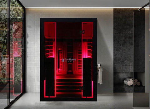 Sun Home Eclipse 2-person red light infrared sauna glowing red behind its glass front, mounted against a wall with a white towel hanging beside it