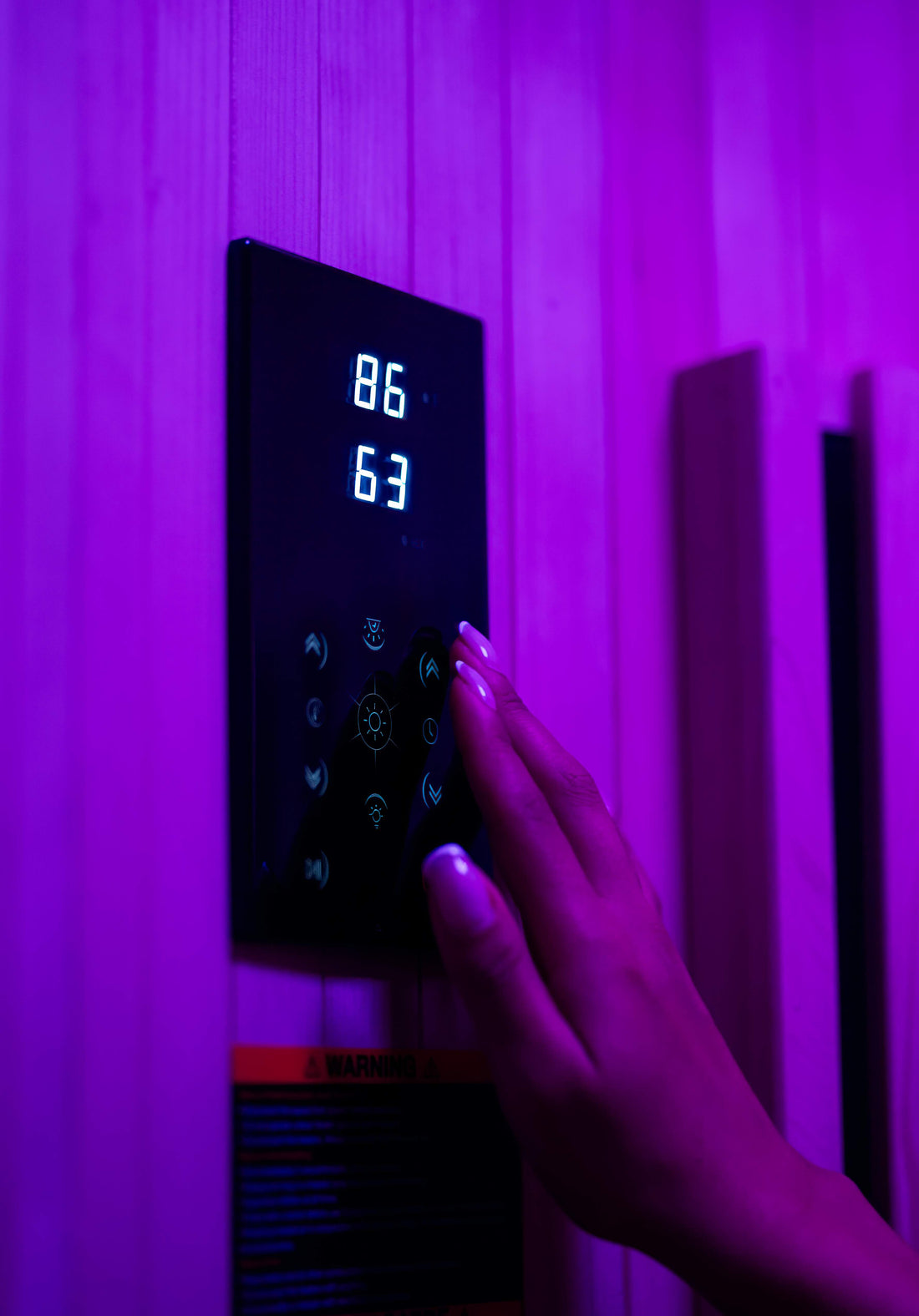 Hand adjusting the touchscreen control panel inside a Sun Home Pod infrared sauna, lit purple