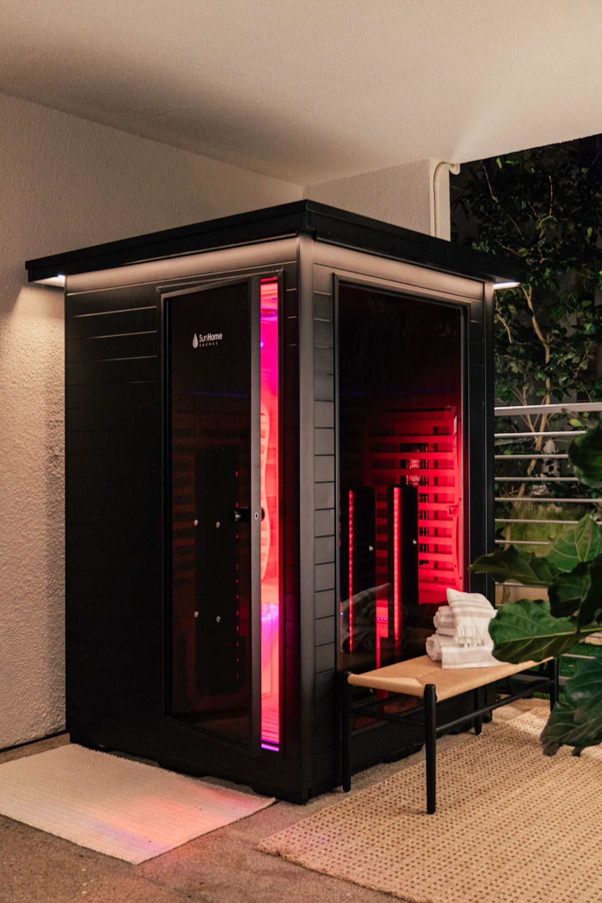 Sun Home Luminar outdoor sauna on a home patio at night with warm glow, towels on a bench