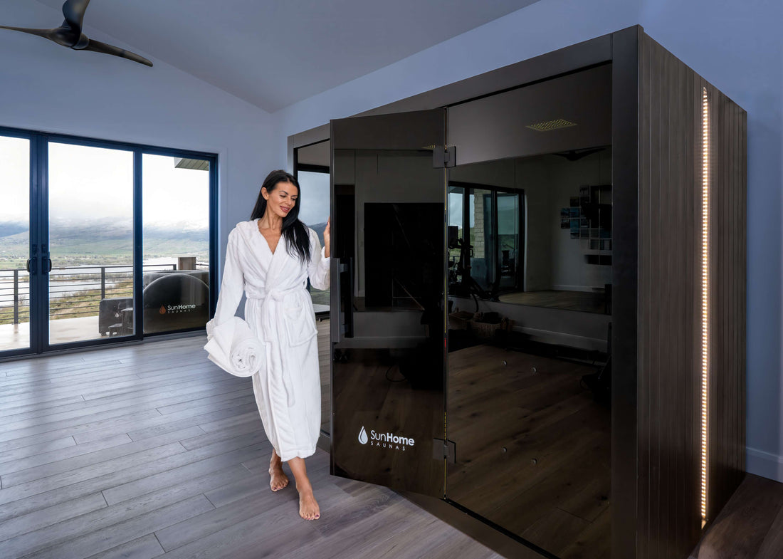 Woman in a robe beside the black-glass Sun Home Eclipse 4-person red light infrared sauna in a modern room