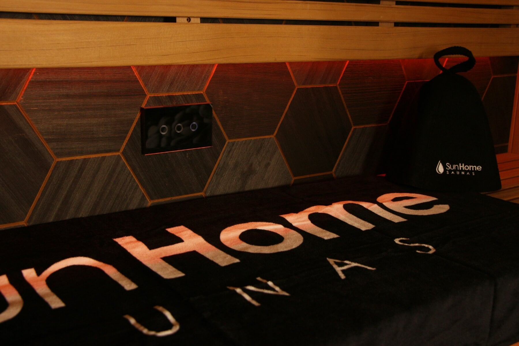 Sun Home Saunas towel and sauna hat resting on a bench in front of a backlit hexagonal wood wall with integrated controls