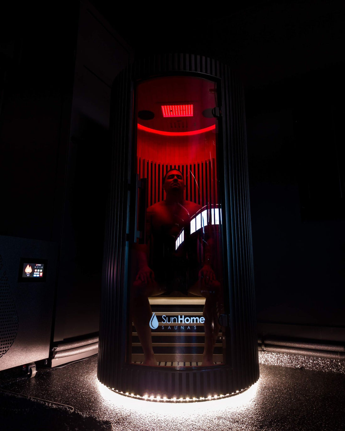 Man seated inside the Sun Home Pod 1-person red light infrared sauna under the red light